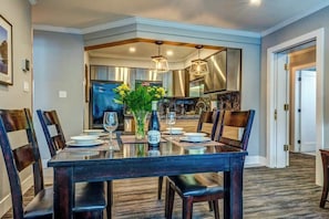 A dining area with a rectangular table set for six, surrounded by chairs, with a vase of flowers on the table.