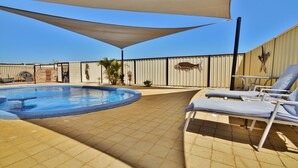 Uma área de piscina com espreguiçadeiras, um espaço de estar coberto e detalhes decorativos nas paredes.