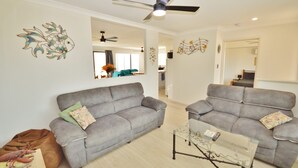 Sala de estar com dois sofás cinzas, uma mesa de centro de vidro e um ventilador de teto.
