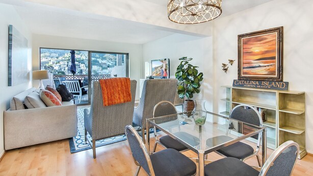 Uma sala de estar moderna com uma mesa de jantar de vidro, assentos confortáveis, uma grande janela com vista para a cidade e um lustre decorativo.