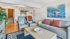 Uma sala de estar moderna com um sofá, cadeiras, uma mesa de centro e um quadro de um barco na água.