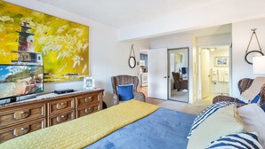 Quarto com cama, cômoda, televisão e quadro de um farol.