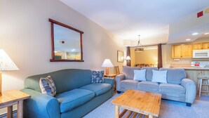 A living room with two sofas, a wooden coffee table, and a kitchen area with a microwave. - Spacious condo that sleeps 4, steps from the lifts, free wifi & parking (Copper Mountain)