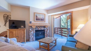 A cozy living room with a stone fireplace, a television on a wooden cabinet, and a sofa. - Spacious condo that sleeps 4, steps from the lifts, free wifi & parking (Copper Mountain)