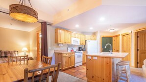 A kitchen with wooden cabinets, a central island, and a dining area with a table and chairs. - Spacious condo that sleeps 4, steps from the lifts, free wifi & parking (Copper Mountain)