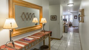 Um corredor com um banco de madeira, duas luminárias na parede, um espelho grande e um tapete estampado.