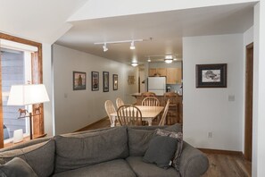 A living room with a sofa, a dining area with a table and chairs, and a kitchen in the background. - Updated & Spacious Ski-In/Ski-Out Condo (Whitefish)
