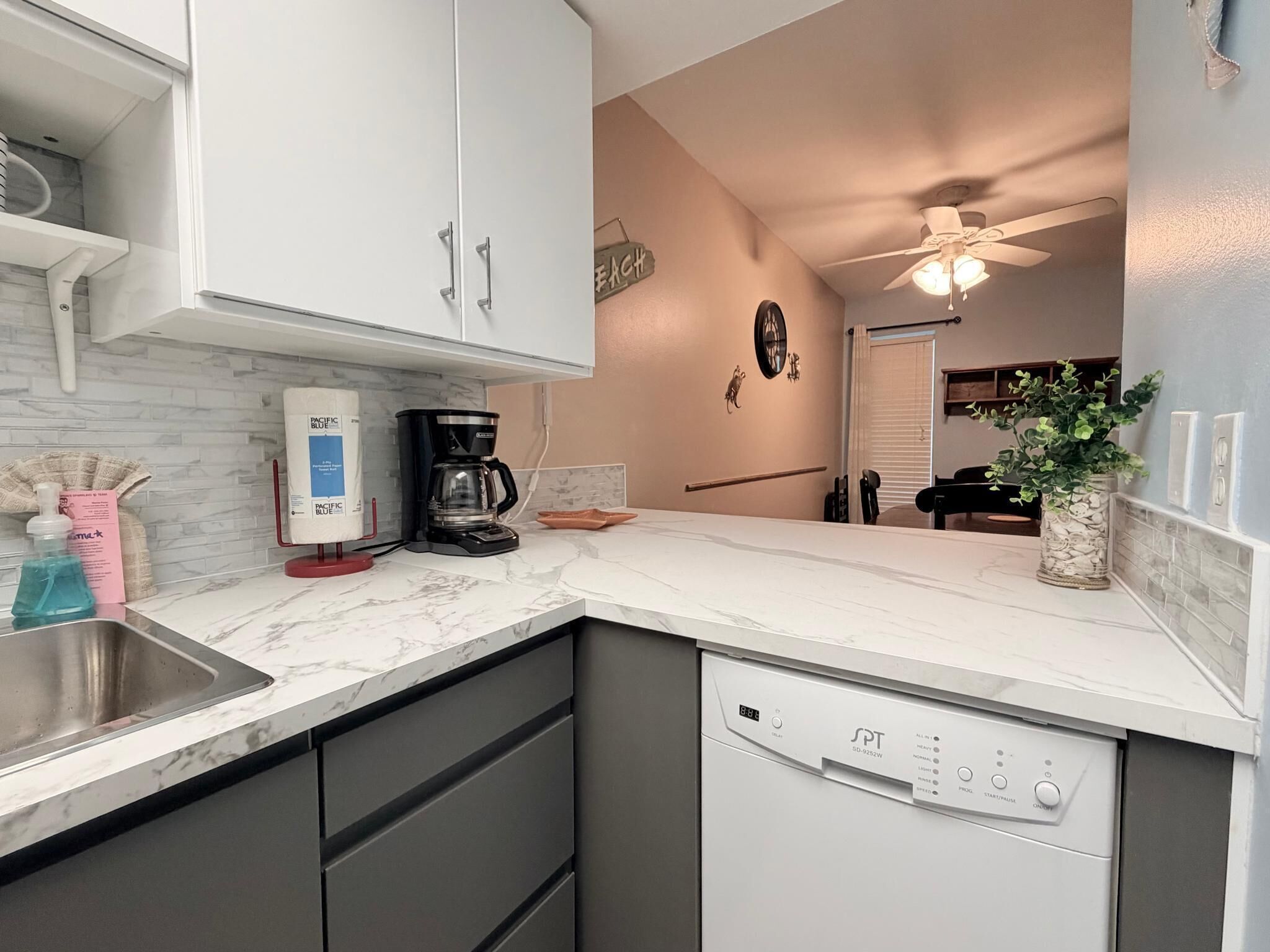 A modern kitchen with a dishwasher, coffee maker, and a marble countertop.