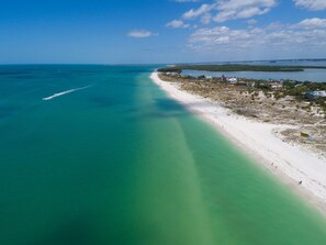 Vista aérea de una playa con aguas turquesas cristalinas, una orilla arenosa y un pequeño poblado con edificios y vegetación.