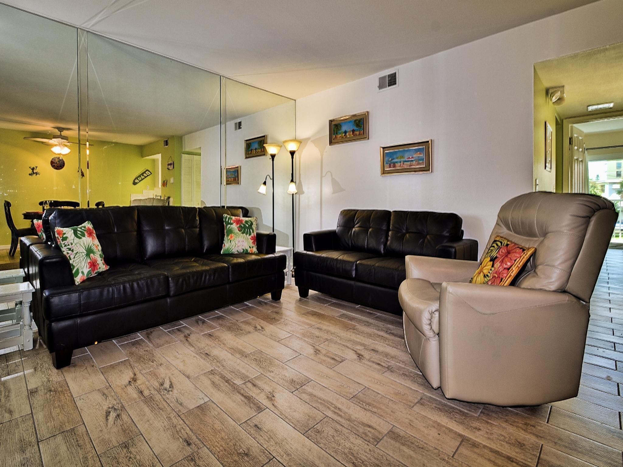 A living room with two black leather sofas, a beige armchair, and a large mirror on the wall.