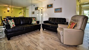 Una sala de estar con dos sofás de cuero negro, un sillón beige y un espejo grande en la pared.