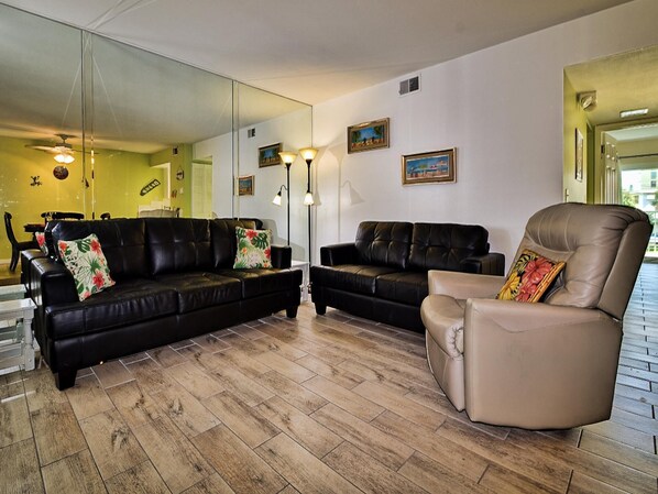 Een woonkamer met twee zwarte leren banken, een beige fauteuil en een grote spiegel aan de muur.