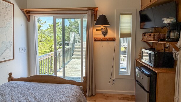 A bedroom with a bed, a TV, a microwave, and a view of a deck and outdoor area. - Follow The Heron: Fantastic home with lots of decks. (Ocracoke)