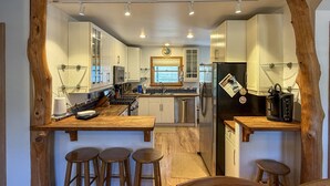 A modern kitchen with white cabinets, a central island with stools, and a refrigerator. - Follow The Heron: Fantastic home with lots of decks. (Ocracoke)