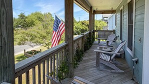A wooden porch with a railing, a flag, and two rocking chairs. - Follow The Heron: Fantastic home with lots of decks. (Ocracoke)