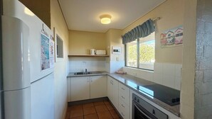 Une cuisine compacte avec des meubles blancs, un four encastré, un évier et une fenêtre donnant sur les voitures garées à l’extérieur.