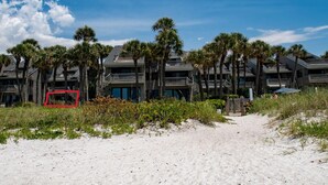 Ein Strandhotel mit mehreren Balkonen, Palmen und einem Sandweg, der zum Eingang führt.