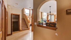A hallway with wooden flooring, a staircase, and a large arched window with a view of the outdoors.