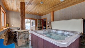 A wooden interior with a hot tub, stone seating, and a view through a glass door.