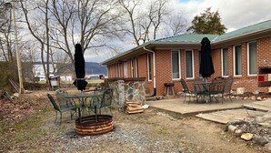 Une terrasse extérieure avec un bâtiment en briques, une table et des chaises en métal, et un foyer.
