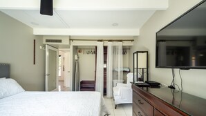 Un dormitorio con cama, cómoda, televisor y baño a la vista a través de una puerta abierta.