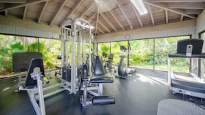 Un gimnasio con diversos equipos de ejercicio, ventanas amplias y techo de madera.
