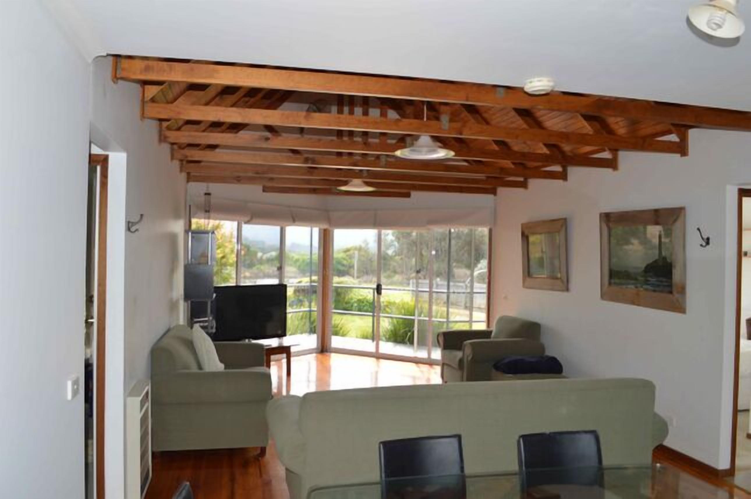 Un salon spacieux doté d’un plafond en bois, d’une porte vitrée donnant sur un balcon et d’un téléviseur à écran plat.