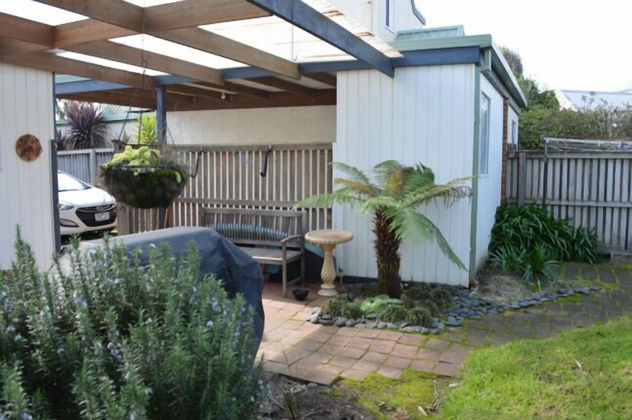 A covered patio area with a hanging planter, a small table, and a palm tree.