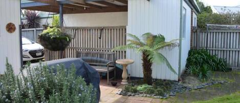 A covered patio area with a hanging planter, a small table, and a palm tree.