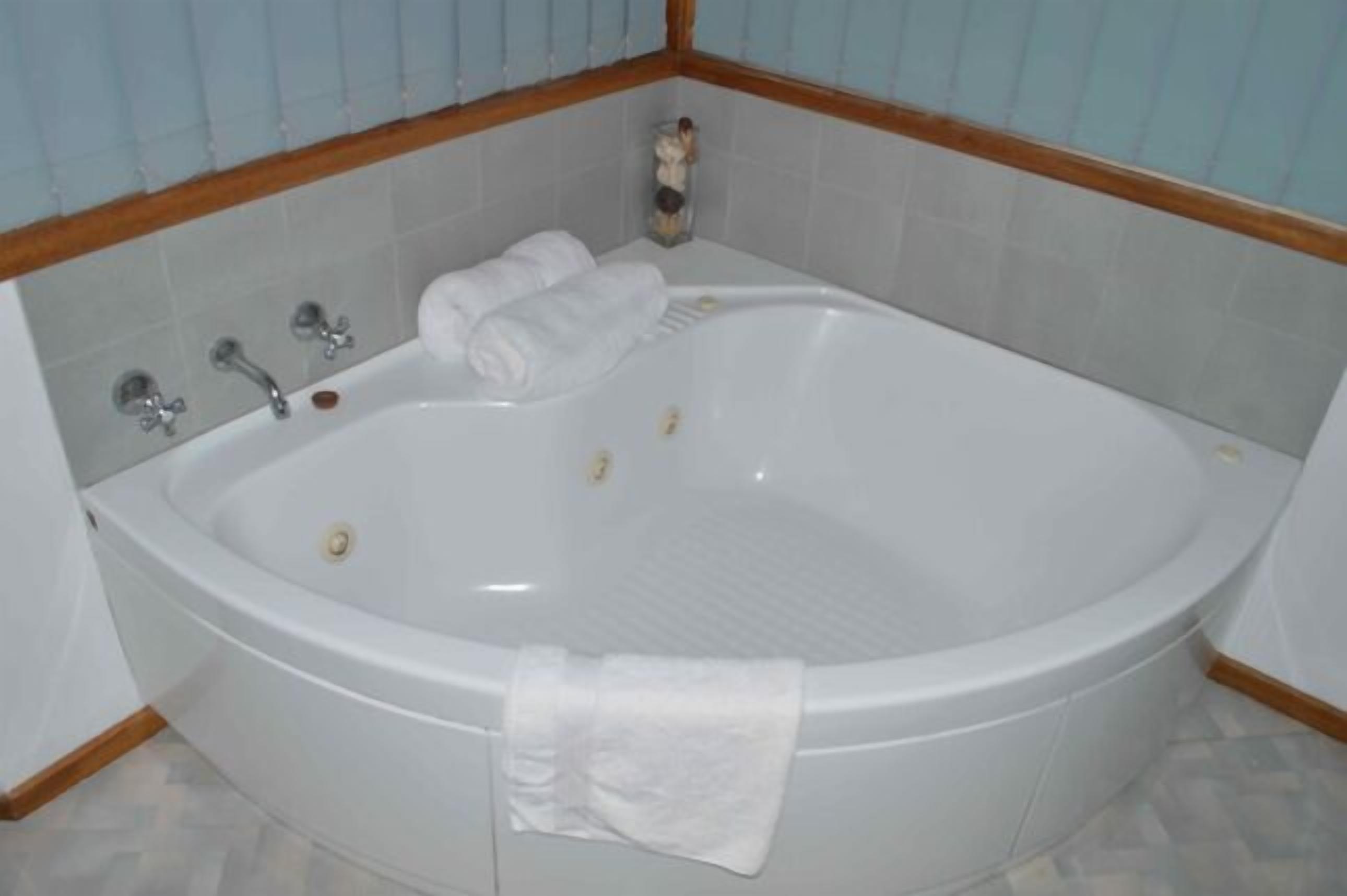 Une grande baignoire de forme ovale, dotée de deux robinets et d’un petit bouton de commande. Deux serviettes blanches sont posées sur le bord de la baignoire.