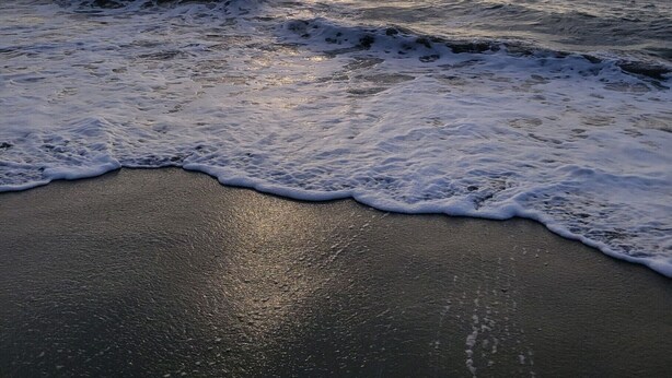 Een strand met golven en een bewolkte lucht.