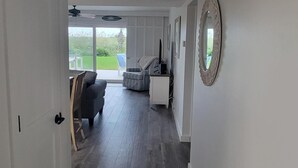 Een hal met een deur links, een plafondventilator, een grote spiegel rechts en een uitzicht op een terras met tuinmeubilair.