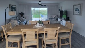 Een eethoek met een houten tafel en stoelen, een plafondventilator en uitzicht op de omgeving door grote ramen.