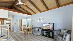 A living room with a dining area, wooden ceiling beams, a flat-screen TV, and a fireplace.