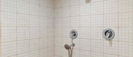 A tiled shower with a handheld showerhead and two wall-mounted faucets.
