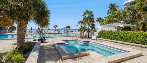 A pool area with multiple swimming pools, palm trees, and a building in the background.