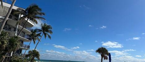 A beach with white sand, palm trees, and a building with balconies overlooking the ocean.