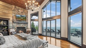 Un dormitorio amplio con una cama grande, una chimenea y vistas al exterior a través de amplios ventanales.