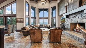 Un salón espacioso con chimenea de piedra, ventanas amplias y un techo alto con vigas a la vista.
