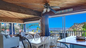 A spacious living area with a dining table and chairs, a sofa, and large windows offering a view of the ocean. - Cozy 2 Bedroom Home with GOLF CART, Stunning View, Balcony, Grill, Wifi - 124 Hi (Avalon)