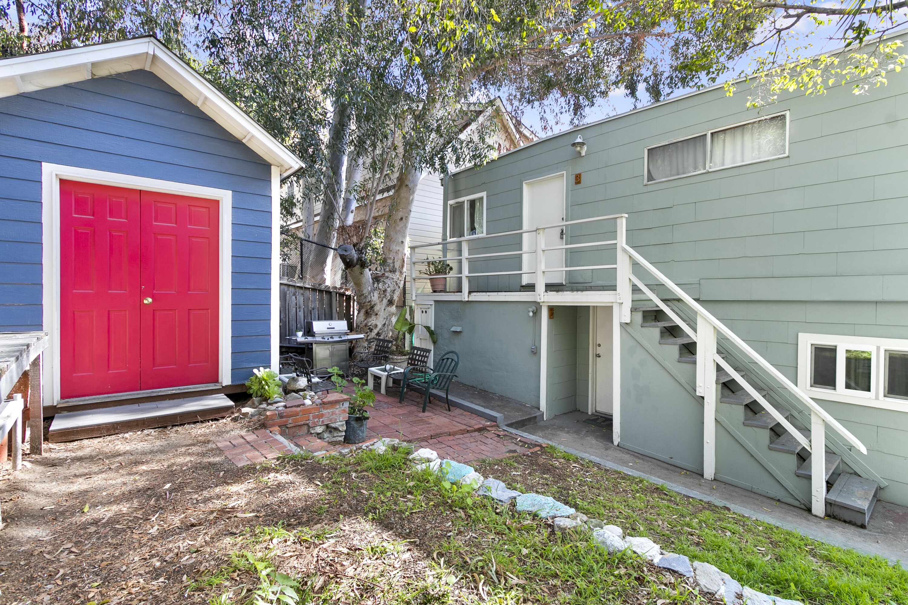 A small house with a red door, a covered patio, and a staircase leading to a second floor.