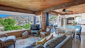A spacious living area with a large TV, comfortable seating, and a view of a mountainous landscape. - Cozy 2 Bedroom Home with GOLF CART, Stunning View, Balcony, Grill, Wifi - 124 Hi (Avalon)