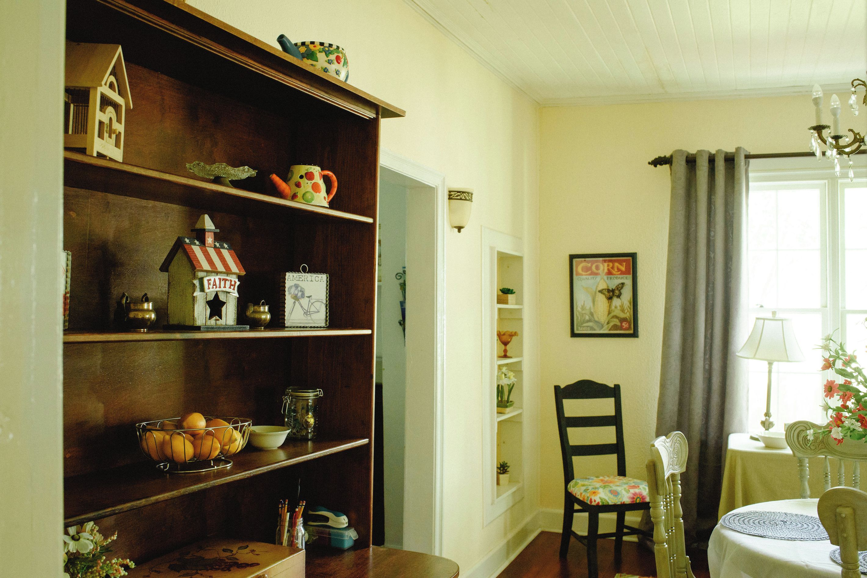 Una habitació amb una estanteria de fusta, una taula de dinar amb cadires i una finestra amb cortines.