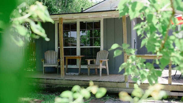 A wooden deck with two Adirondack chairs and a small table, surrounded by a wooden fence and greenery. - The Original Crafter's Cottage Convenient to Savannah (Bloomingdale)