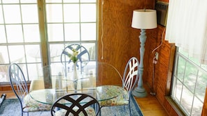 A dining area with a glass table, chairs, a vase with flowers, a lamp, and a view through large windows. - The Original Crafter's Cottage Convenient to Savannah (Bloomingdale)