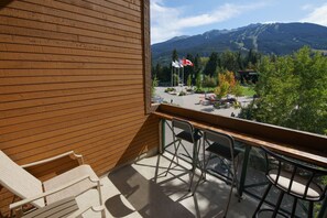 A balcony with a view of a mountainous landscape, a flagpole with flags, and outdoor seating. - Marketplace Lodge 333 (Whistler)