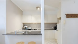 Una cocina moderna con armarios blancos, encimera negra y dos taburetes de madera.