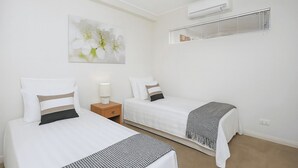 Una habitación de hotel con dos camas, una mesita de noche con lámpara, un aire acondicionado y una ventana con persianas.