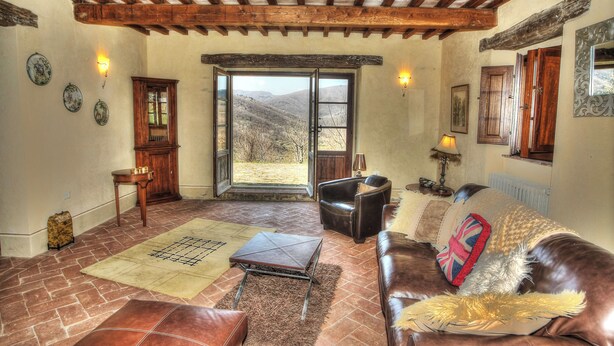 A cozy living room with a leather sofa, a coffee table, and a view through a large window. - Beautifully converted farmhouse alone on a tuscan hillside with stunning views (Cortona)