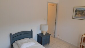 A bedroom with a bed, a nightstand with a lamp, a door, and a framed picture on the wall. - F9 Large bright apartment, 3 rooms, beach at 50m, swimming pool and sea view  (Théoule Sur Mer)